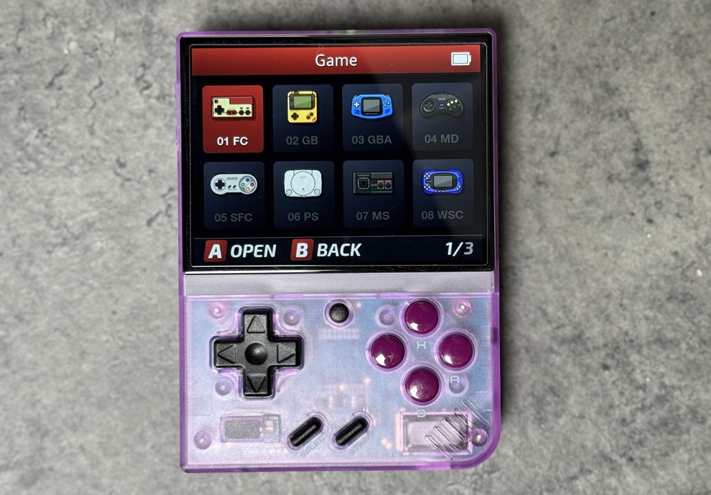 Miyoo Mini Plus console rétro affichant l’écran de sélection des jeux, incluant des émulateurs pour NES, Game Boy, GBA et PlayStation, avec un design violet transparent.